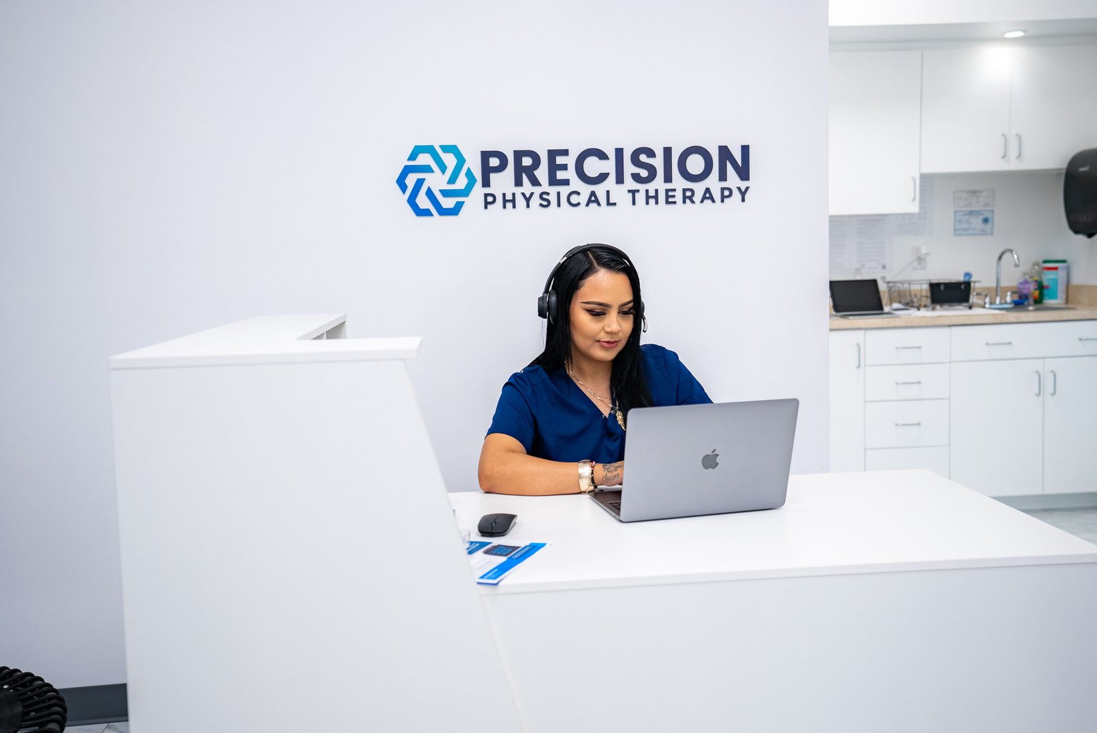 A receptionist working on a computer at the check in desk at Precision Physical Therapy.