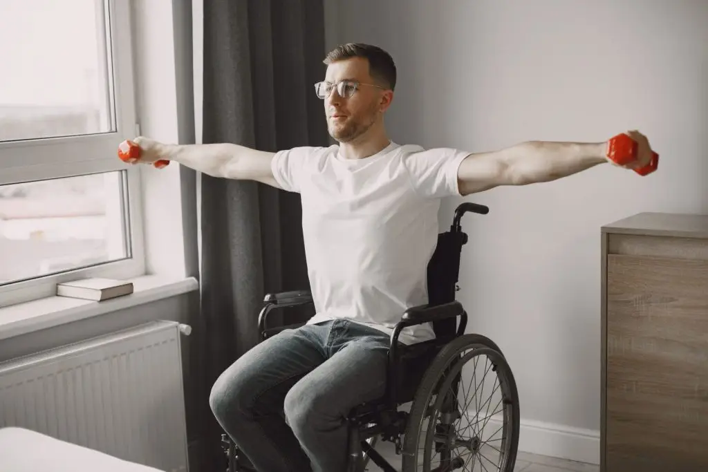 Man in wheelchair lifting red dumbbells in a bright room, promoting inclusive fitness.